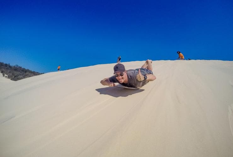 Meluncur dengan tobogan di bukit pasir, Moreton Island Desert, Moreton Island, QLD © Tourism Australia