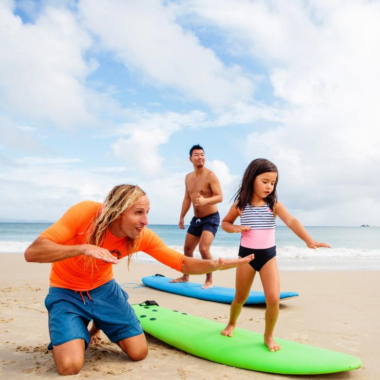 Keluarga belajar berselancar di Clarkes Beach, Byron Bay. © Destination NSW