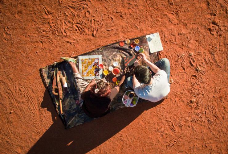 Pemandangan dari atas pengunjung yang belajar melukis titik dengan seniman Aborigin lokal dari Maruku Arts di dekat Uluru di Northern Territory © Tourism NT/Archie Sartracom