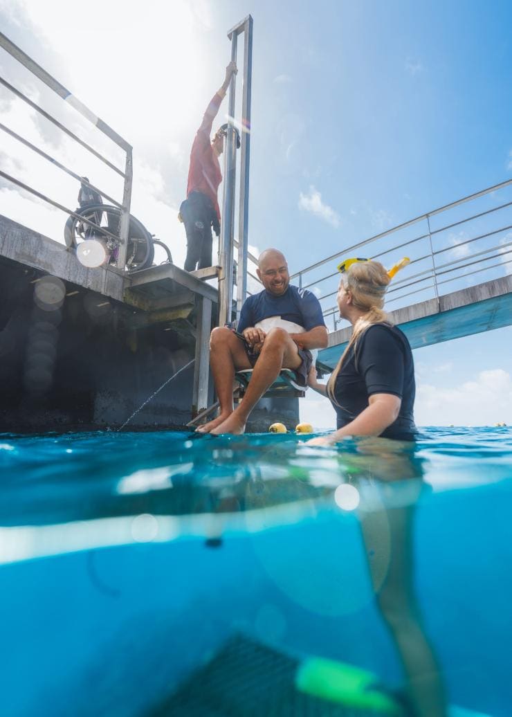 Ein Mann mit eingeschränkter Mobilität wird mit einem Lift vom einem Boot von Quicksilver Cruise in den Ozean heruntergelassen, Great Barrier Reef, Queensland © Tourism and Events Queensland