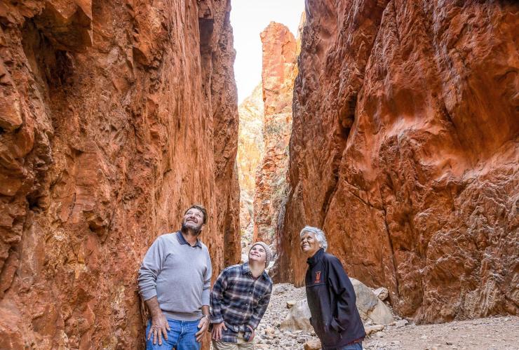 Ein Mann mit einer neurologischen Behinderung, ein Reiseleiter und ein anderer Mann blicken bei Standley Chasm nach oben, West MacDonnell Ranges, Northern Territory © Tourism NT/Helen Orr