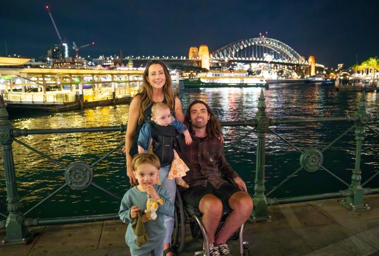 Seorang pria yang duduk di kursi roda bersama keluarganya di Circular Quay, Sydney, New South Wales © Tourism Australia