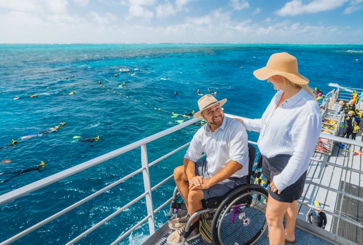 Seorang pria duduk di kursi roda dengan pasangannya di kapal Quicksilver Cruise, Great Barrier Reef, Queensland © Tourism and Events Queensland