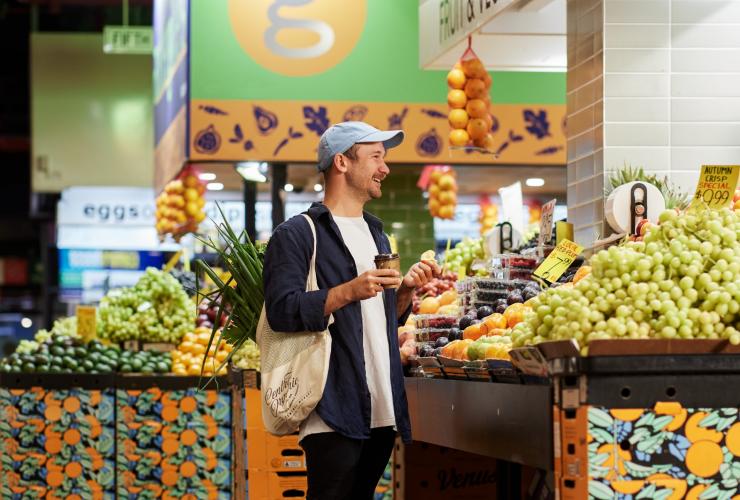 A person standing at a stall brimming with colourful fruit while holding a coffee at Adelaide Central Market, Adelaide, South Australia © South Australian Tourism Commission