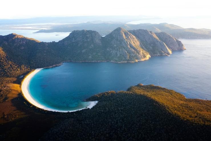 Aerial view of Wineglass Bay and the surrounding mountains covered with trees at Freycinet National Park, Tasmania © Lauren Bath