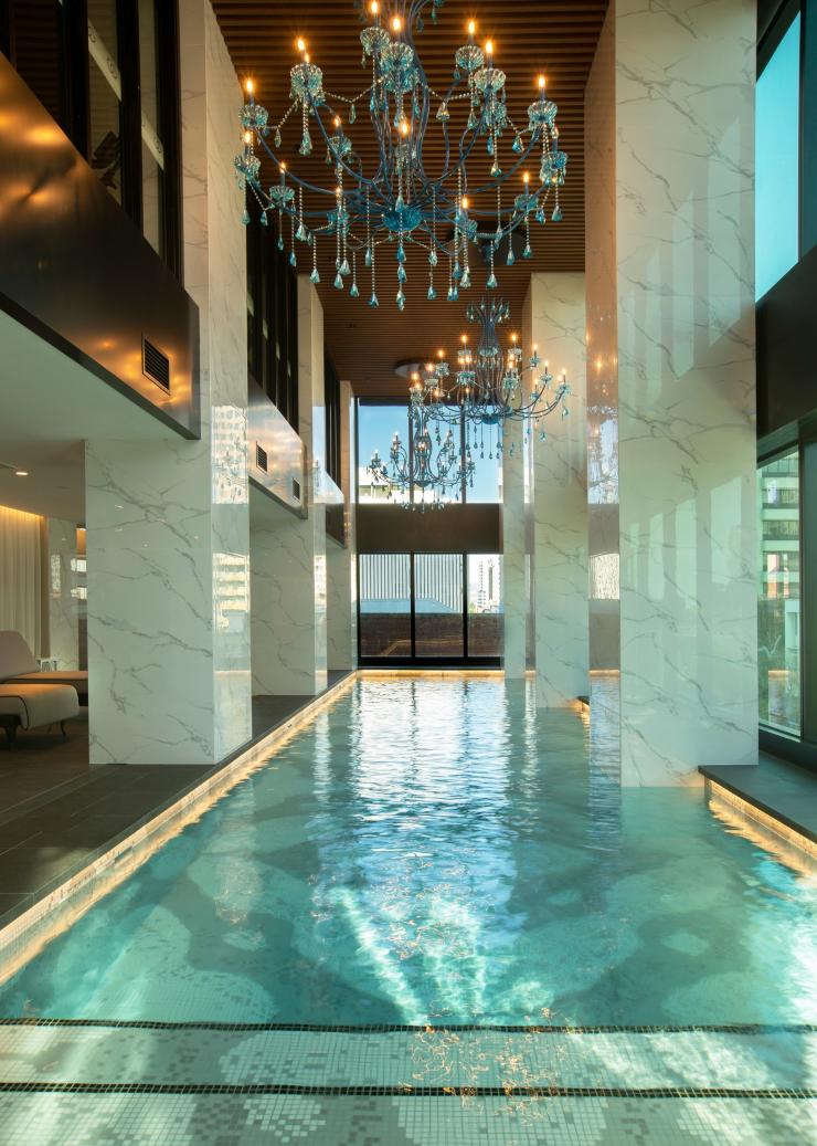 A sparkling turquoise pool inside a building with tall ceilings, white marble pillars and blue chandeliers at Sofitel Adelaide, Adelaide, South Australia © Sofitel Adelaide