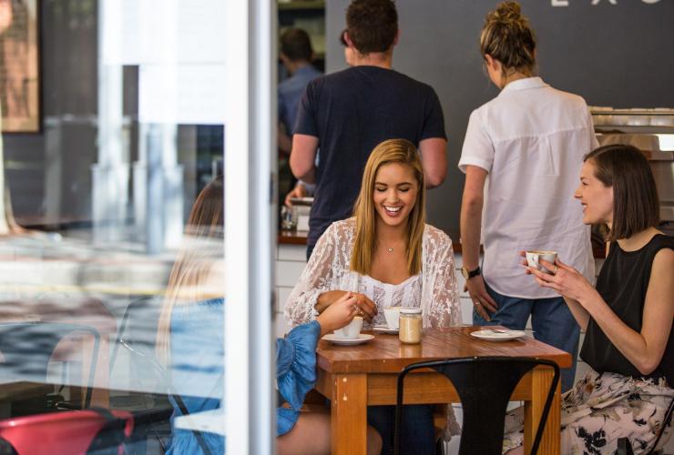 A group of friends smiling and talking over coffee in a bustling cafe at Exchange Specialty Coffee, Adelaide, South Australia © South Australian Tourism Commission