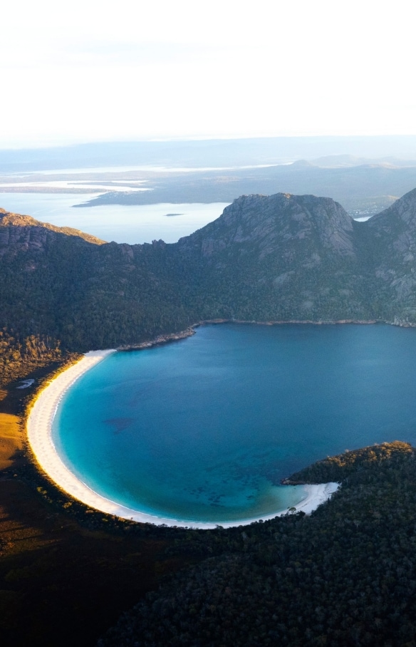 Aerial view of Wineglass Bay and the surrounding mountains covered with trees at Freycinet National Park, Tasmania © Lauren Bath