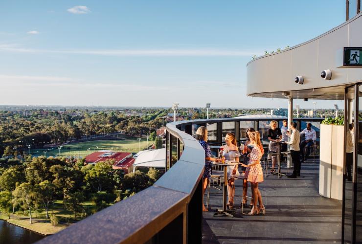 A group of friends gathered around a table sipping drinks on a rooftop overlooking suburbs and bushland at SOL Rooftop, Adelaide, South Australia © Meaghan Coles