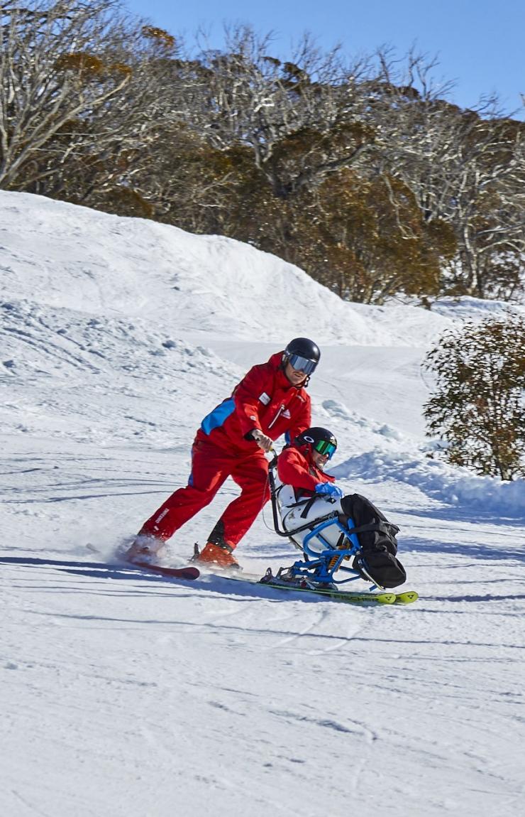 Two people with limited mobility adaptive skiing with instructors down a snow-covered mountain in Thredbo, Snowy Mountains, New South Wales © Tourism Australia