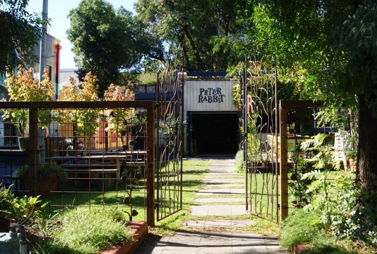 Iron gates open to a pathway through a lush green garden with picnic tables, leading to a building with a sign reading 'Peter Rabbit', Adelaide, South Australia © James McIntyre