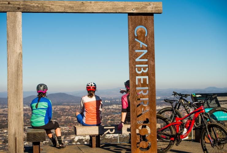 Eine Gruppe von Radfahrern macht auf dem Centenary Trail Rast an einem Aussichtspunkt mit Blick auf die Stadt, Canberra, Australian Capital Territory © Damian Breach/VisitCanberra