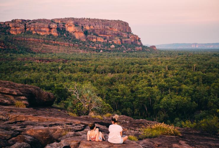 Zwei Personen sitzen auf einer Felsklippe und blicken auf die weite grüne Landschaft, Burrungkuy (Nourlangie) Rock, Kakadu National Park, Northern Territory © Tourism NT/Jewels Lynch