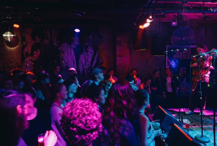 Eine Menschenmenge beobachtet den Auftritt einer Band auf der Bühne unter bunten Lichtern in einem schwach beleuchteten Raum, Cherry Bar, Melbourne, Victoria © Visit Victoria
