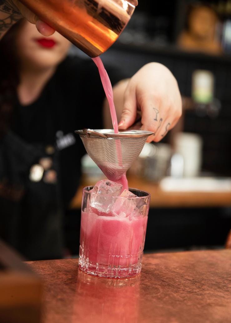 Eine Barkeeperin schenkt einen leuchtend pinkfarbenen Cocktail in der Four Pillars Gin Distillery ein, Yarra Valley, Victoria © Visit Victoria