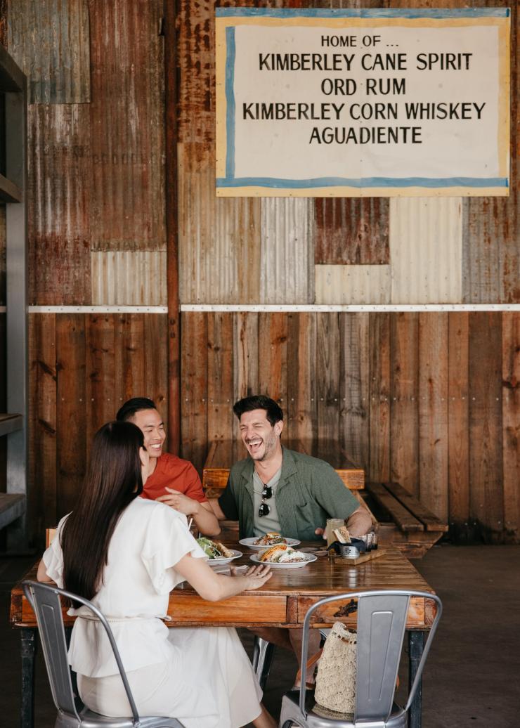 Drei Freunde sitzen um einen Tisch mit Essen im Hoochery Distillery Café, Kununurra, Westaustralien © Tourism Western Australia