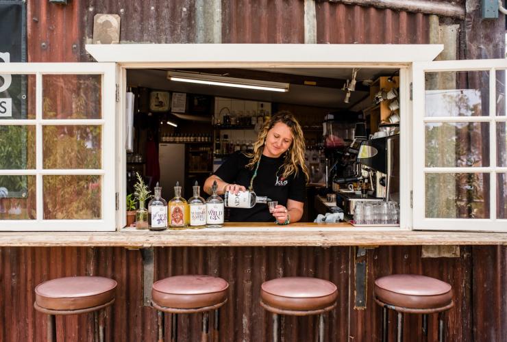 Eine Barkeeperin gießt in einem mit Barhockern gesäumten Fenster Alkohol in ein Glas, Kangaroo Island Spirits, Kangaroo Island, Südaustralien © Meaghan Coles