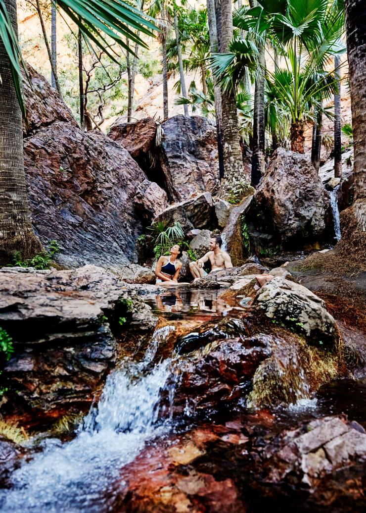 Ein Paar sitzt entspannt inmitten der Wasserfälle von Zebedee Springs, El Questro Wilderness Park, Westaustralien © Tourism Western Australia