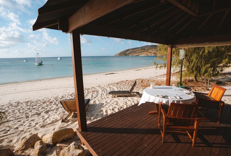 Eine Cabana aus Holz mit einem Esstisch über weißem Sand, der zum blauen Meer führt, Lizard Island Resort, Lizard Island, Queensland © Tourism Australia