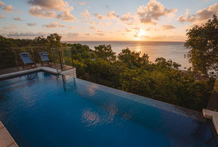 Blick auf einen großen Infinity-Pool, grüne Bäume und den Sonnenuntergang über dem darunterliegenden Ozean, Lizard Island Resort, Lizard Island, Queensland © Tourism Australia