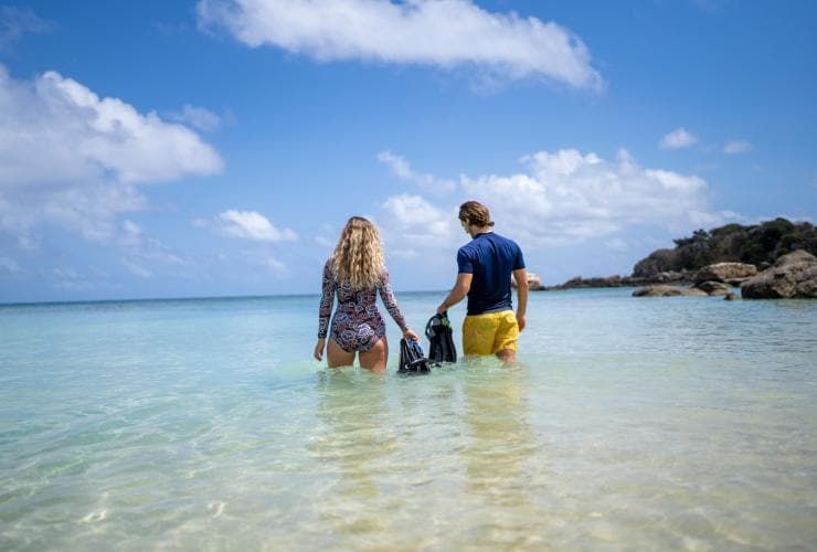 Ein Mann und eine Frau gehen mit Flossen und Schnorcheln in das klare blaue Wasser, Lizard Island Resort, Lizard Island, Queensland © Tourism and Events Queensland