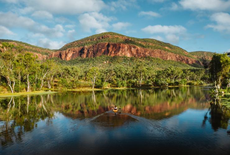 Eine Person fährt an einem sonnigen Tag mit dem Kajak auf einem stillen Wasser, umgeben von Bäumen und felsigen Bergen, Mt. Mulligan Lodge, Mount Mulligan, Queensland © Mount Mulligan Lodge
