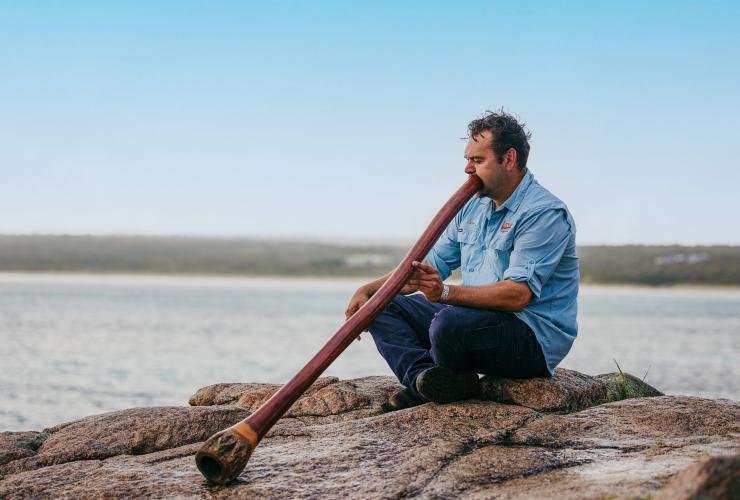 An Aboriginal man sits atop a rock playing the didgeridoo in Australia's South West, Western Australia © Tourism Australia