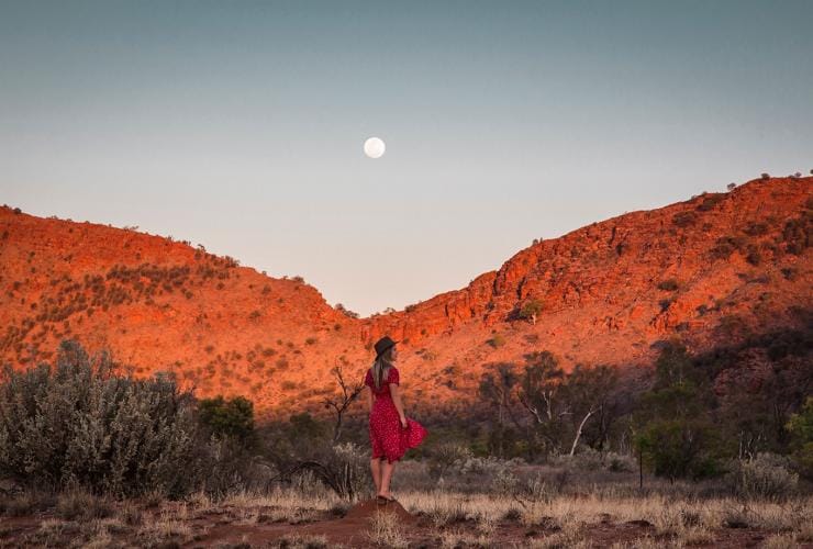 A woman standing in front of bright red rocks in the West Macdonnell Ranges, Northern Territory © Tourism Australia