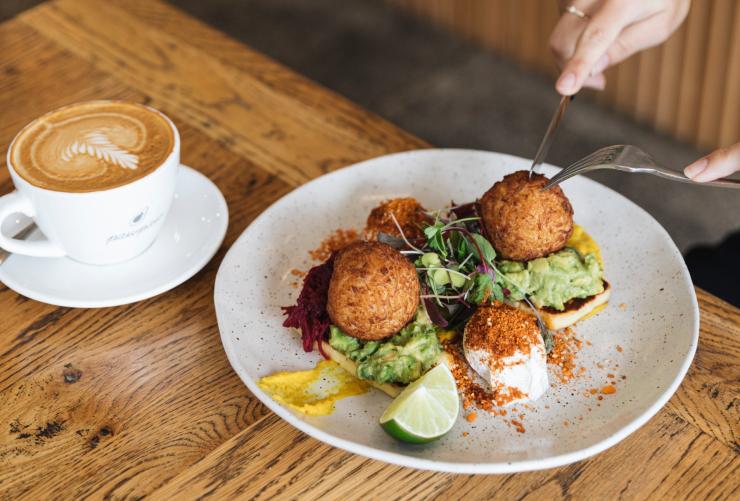 A person cutting into a decadent fried ball of cheese on top of avocado toast with a coffee to their side at Pawpaw Cafe, Brisbane, Queensland © Pawpaw Cafe