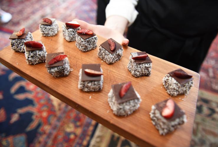A person holding a tray of lamingtons topped with chocolate and fruit at The Great Aussie Brunch, World's 50 Best Restaurants © Tourism Australia