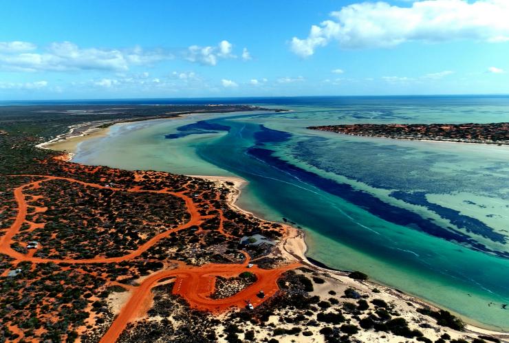 Aerial view over the swirling blue waters of Big Lagoon surrounded by deep red sand and plants in Shark Bay World Heritage Area, Western Australia © Australia’s Coral Coast