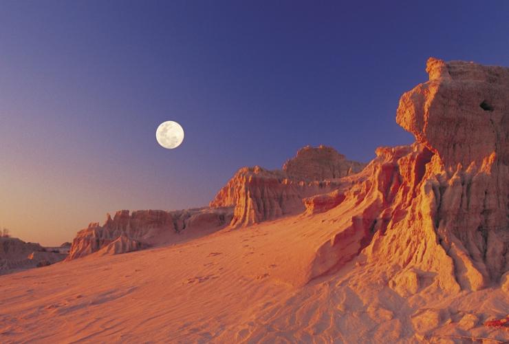 Tall clay and sand formations known as the Walls of China rising towards the night sky with a full moon above them, Mungo National Park, New South Wales © Destination NSW