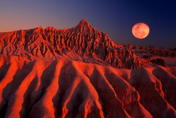 The ridged sand and clay formations of Mungo National Park glowing red beneath the light of a full moon, New South Wales © Tourism Australia