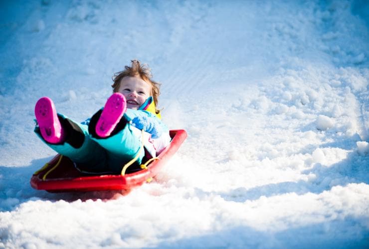 Child riding down a snowy hill on a toboggan at Corin Forest, Paddys River, Australian Capital Territory © Visit Canberra