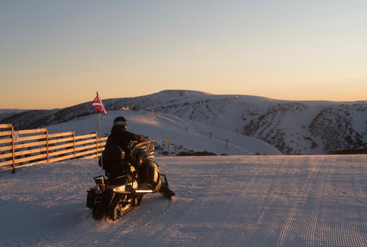 Person riding a snowmobile on top of a mountain during sunrise at Mount Hotham, Victoria © Hotham Alpine Resort