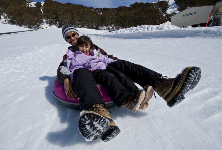 A child and parent riding down a tube on a snowy slope at Falls Creek, Victoria © Visit Victoria