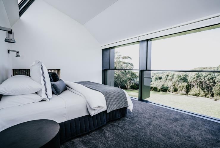 A bedroom with sleek, monochromatic furnishings and a large bed overlooking views of lush greenery at Alkina Lodge, Wattle Hill, Victoria © Alkina Lodge