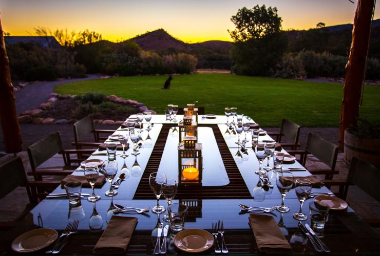 An outdoor dining table in the foreground beautifully set with candles in the middle and grassy bushland beyond at Arkaba Station Homestead, Flinders Ranges, South Australia © Wild Bush Luxury / Great Walks of Australia