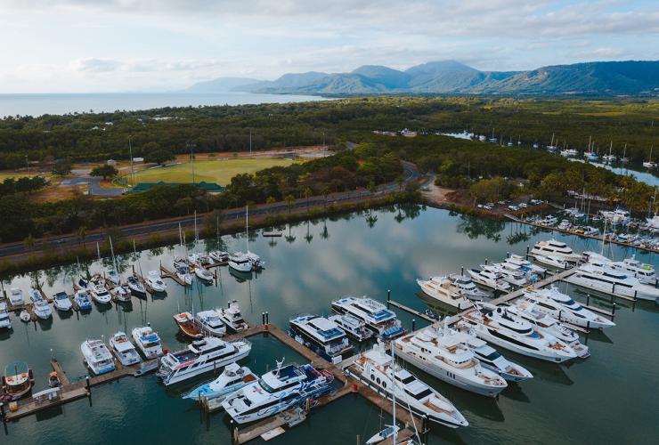Aerial view over a marina lined with boats and lush green mountains bordering the ocean in the distance at Four Mile Beach, Port Douglas, Queensland © Tourism Australia