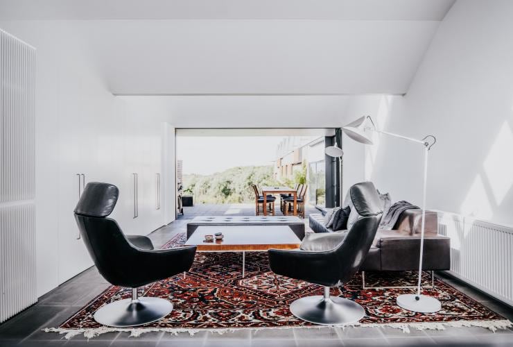 The interior of a lounge room with a cosy patterned rug and sleek furnishings leading to a large outdoor balcony and dining table at Alkina Lodge, Wattle Hill, Victoria © Alkina Lodge