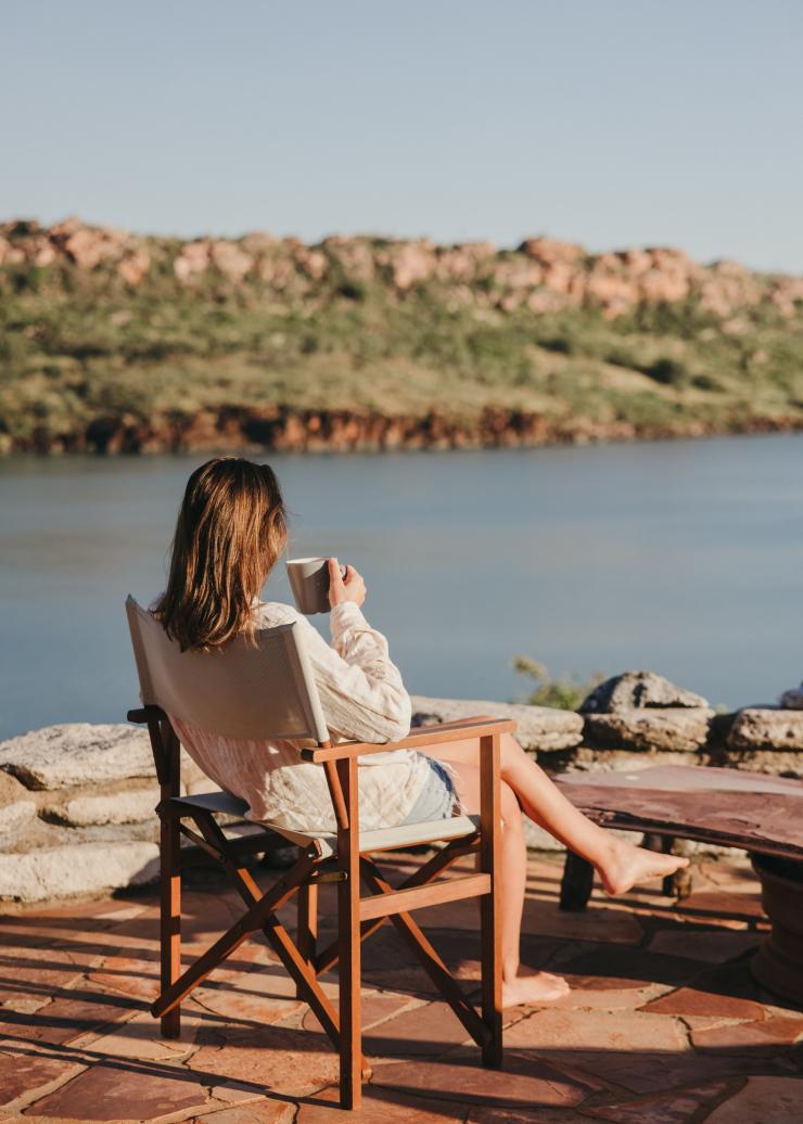A woman sitting on a chair overlooking the ocean while sipping from a mug at Faraway Bay, the Kimberley, Western Australia © Tourism Western Australia