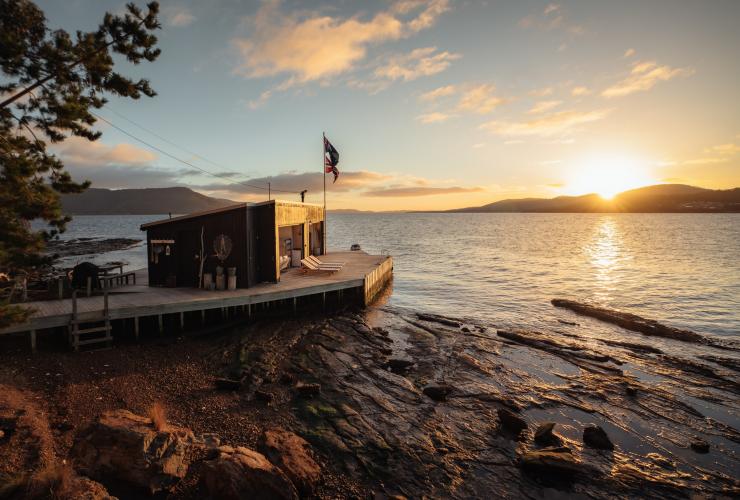 Sunset over the water and distant mountains with waterside holiday accommodation in the forefront on Satellite Island, Tasmania © Jason Charles Hill