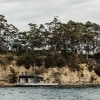 View across the water towards waterfront accommodation, rock faces and greenery on Satellite Island, Tasmania © Adam Gibson