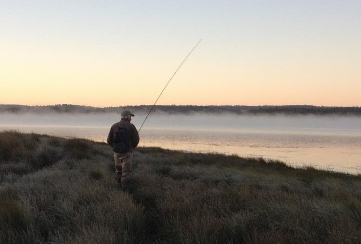 Man fishing from the banks of a misty lake at sunset, Central Highlands, Tasmania © Driftwater