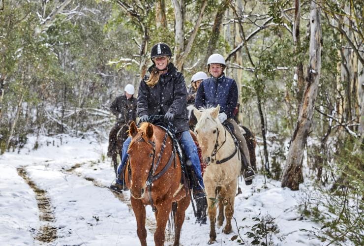 Close-up of a person smiling among a group of people riding horses through the snowy bushland at Thredbo Valley Horse Riding, Snowy Mountains, New South Wales © Tourism Australia