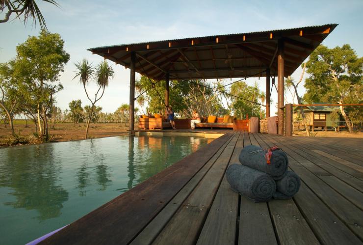 Two people sitting beneath a cabana beside a pool using binoculars to look out across wetlands at Bamurru Plains, Kakadu National Park, Northern Territory © Peter Eve