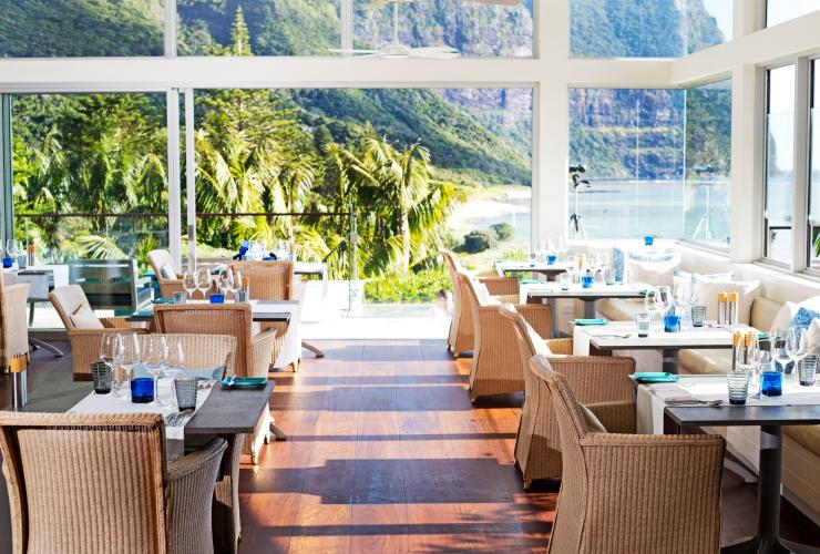 A light-filled restaurant lined with tables and floor to ceiling windows giving way to views of the ocean and rainforest at Capella Lodge, Lord Howe Island, New South Wales © Nathan Dyer