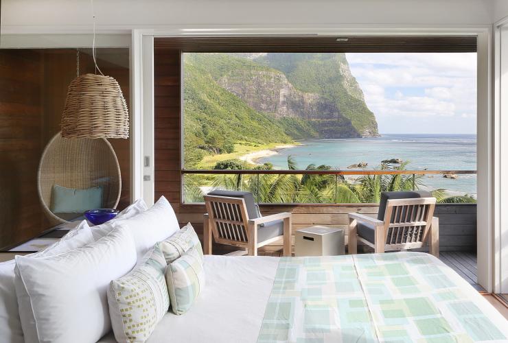 The interior of accommodation complete with a bed, a swing chair and two lounge chairs facing sweeping views over lush greenery and the ocean at Capella Lodge, Lord Howe Island, New South Wales © Rhiannon Taylor