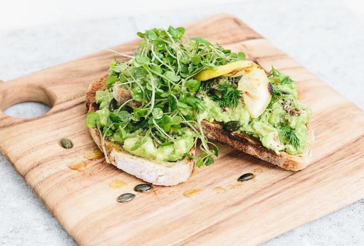 A wooden board with avocado toast topped with herbs at Smashed avocado on toast, Folk cafe, Byron Bay, New South Wales © Folk Cafe