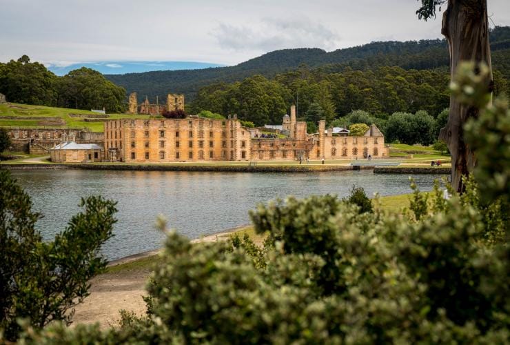 Trees in the foreground with the green grounds and structure of Port Arthur Historic Site visible across a body of water, Port Arthur, Tasmania © Alastair Bett